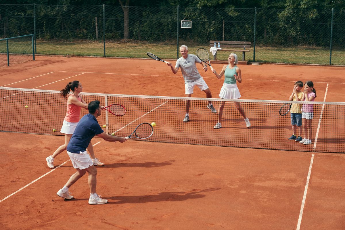 Abuelos, padres y nietos juegan al tenis en una cancha de polvo de ladrillo