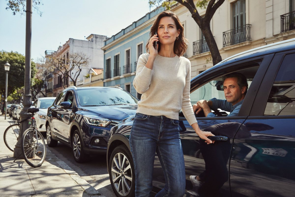Mujer hablando por celular junto a su auto